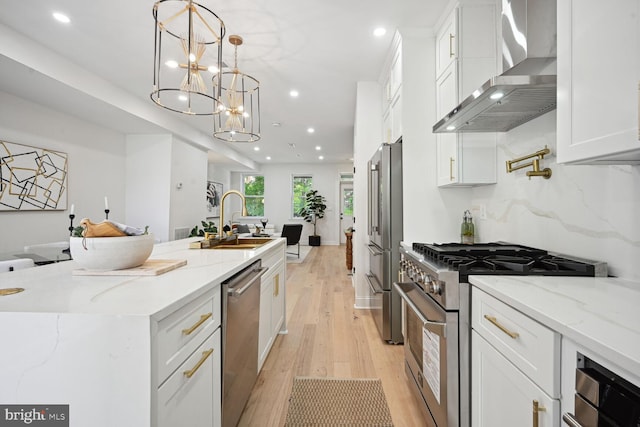 kitchen featuring premium appliances, wall chimney range hood, decorative light fixtures, light hardwood / wood-style floors, and white cabinetry