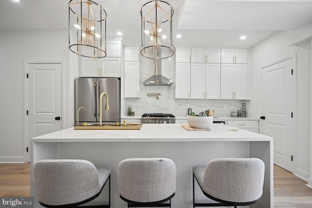 kitchen featuring a center island with sink, white cabinets, light hardwood / wood-style flooring, appliances with stainless steel finishes, and decorative light fixtures