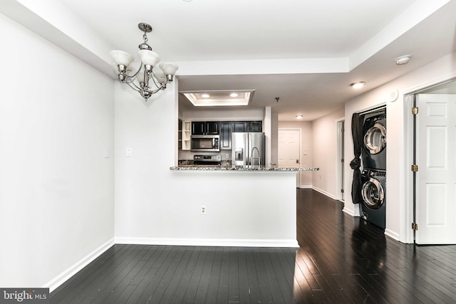 kitchen with stacked washing maching and dryer, stainless steel appliances, a raised ceiling, dark hardwood / wood-style flooring, and kitchen peninsula