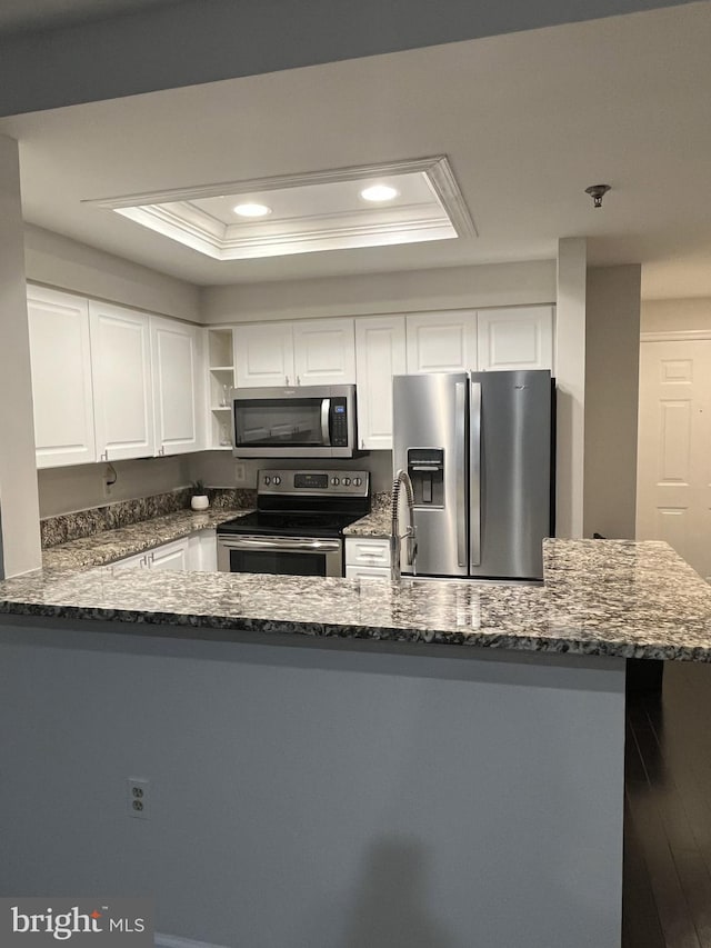 kitchen featuring a raised ceiling, kitchen peninsula, appliances with stainless steel finishes, white cabinets, and hardwood / wood-style flooring