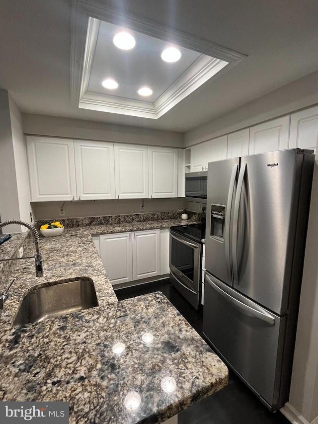 kitchen with sink, stainless steel appliances, dark stone counters, a tray ceiling, and white cabinets