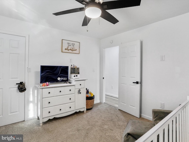 bedroom with a crib, light colored carpet, and ceiling fan