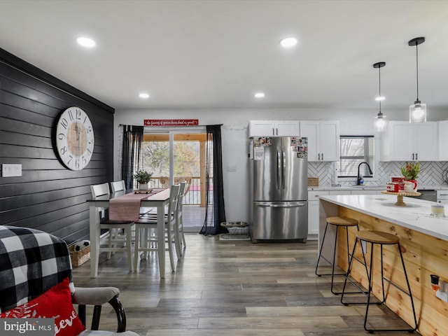 kitchen with stainless steel refrigerator, sink, dark wood-type flooring, hanging light fixtures, and white cabinets