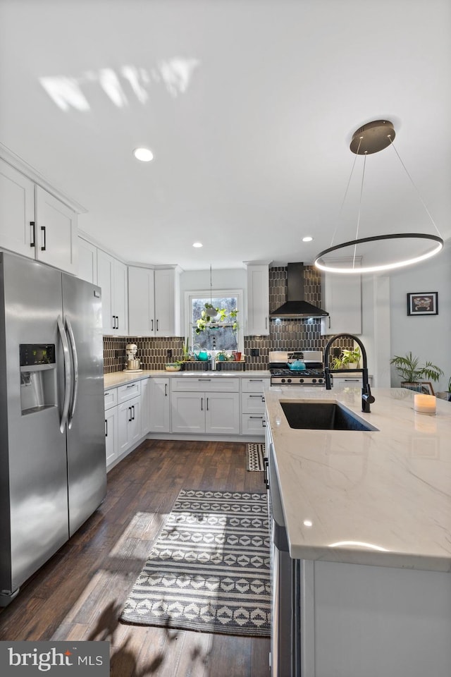 kitchen featuring white cabinetry, dark wood-type flooring, hanging light fixtures, stainless steel appliances, and wall chimney range hood