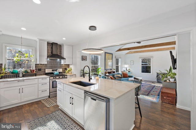 kitchen featuring white cabinets, wall chimney range hood, sink, appliances with stainless steel finishes, and decorative light fixtures