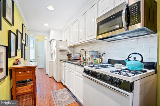 kitchen with light wood-type flooring, ornamental molding, white appliances, sink, and white cabinetry