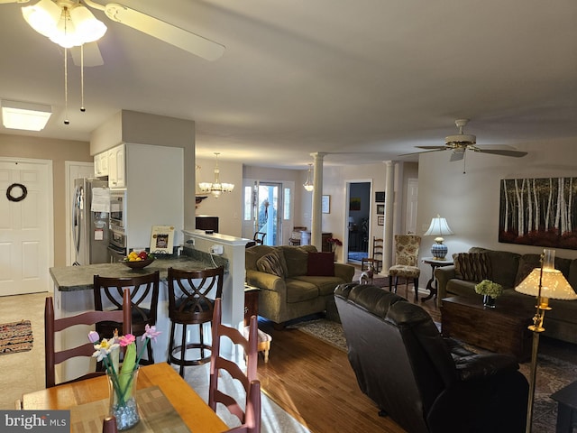 living room featuring decorative columns, wood-type flooring, and ceiling fan with notable chandelier