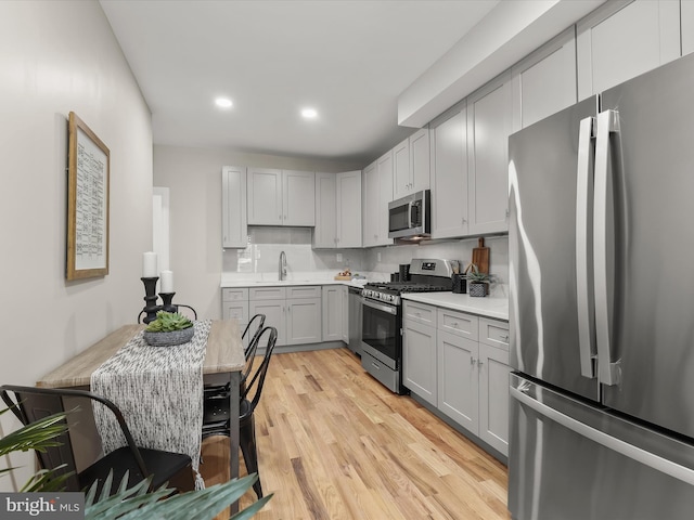 kitchen featuring sink, light hardwood / wood-style flooring, gray cabinetry, backsplash, and stainless steel appliances