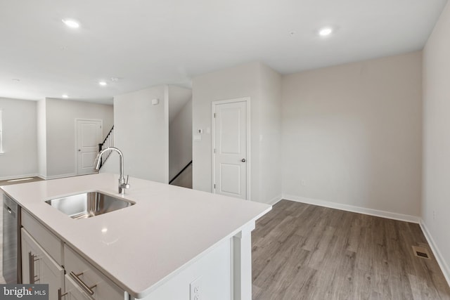 kitchen with sink, stainless steel dishwasher, an island with sink, light hardwood / wood-style floors, and white cabinets