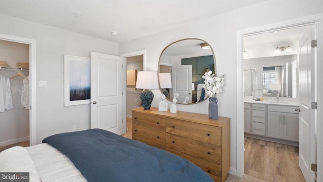 bedroom featuring a walk in closet, light wood-type flooring, ensuite bath, sink, and a closet