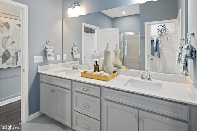 full bathroom with a stall shower, a spacious closet, double vanity, and baseboards