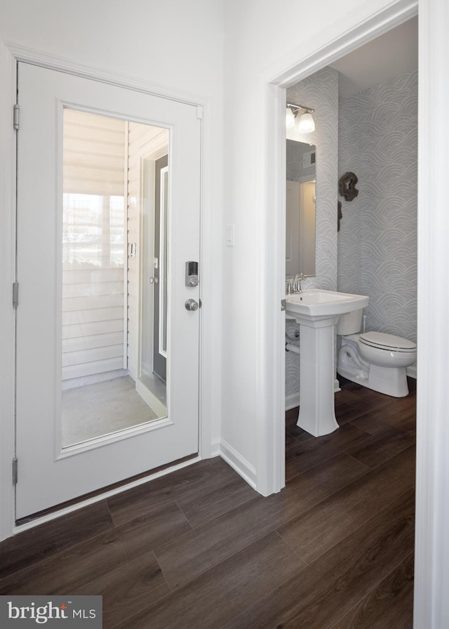 half bathroom with toilet, wallpapered walls, wood finished floors, and baseboards