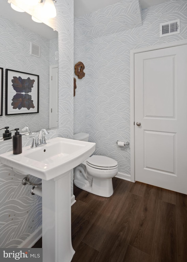 half bath featuring wallpapered walls, toilet, and wood finished floors
