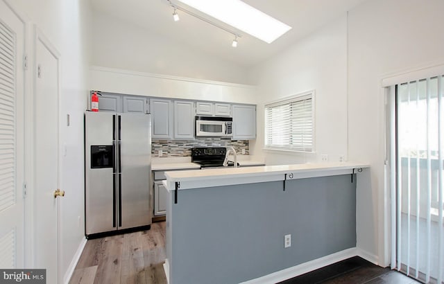 kitchen with kitchen peninsula, vaulted ceiling with skylight, gray cabinets, light wood-type flooring, and stainless steel fridge with ice dispenser