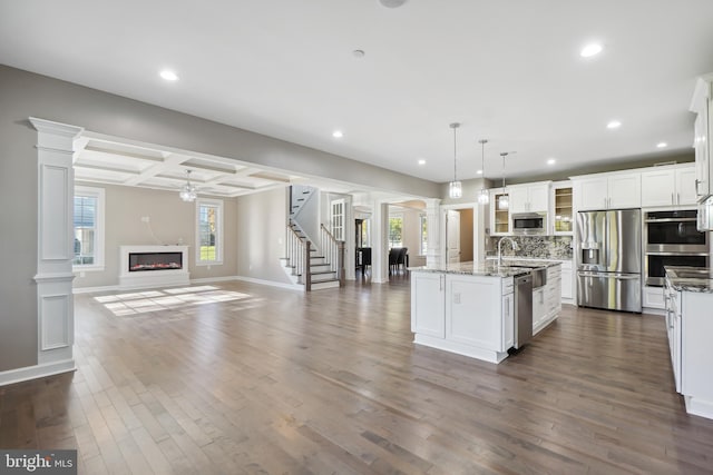 kitchen featuring pendant lighting, stainless steel appliances, a center island with sink, and dark wood-type flooring