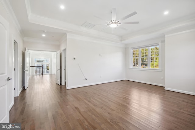 empty room featuring a tray ceiling, crown molding, ceiling fan, and dark wood-type flooring