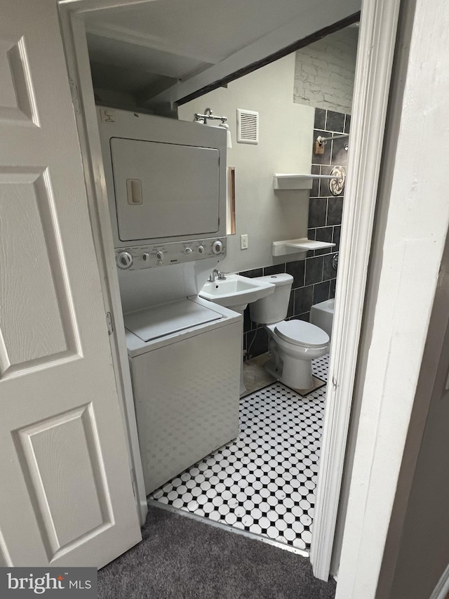 bathroom with toilet, stacked washer and dryer, and tile walls