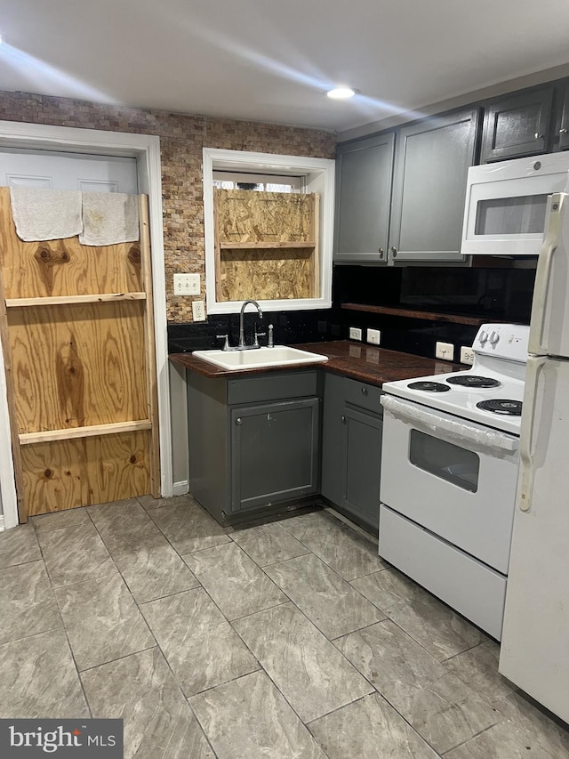 kitchen with backsplash, gray cabinets, sink, and white appliances