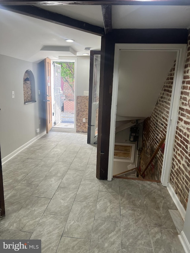 corridor featuring beam ceiling and brick wall