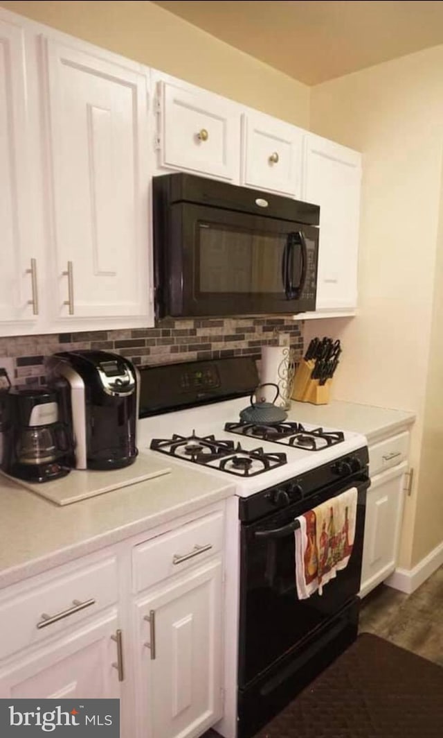 kitchen with tasteful backsplash, white cabinets, black appliances, and dark hardwood / wood-style floors