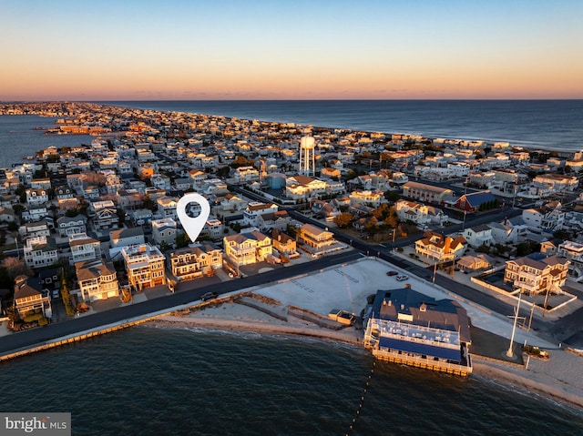 aerial view at dusk featuring a water view and a view of the beach