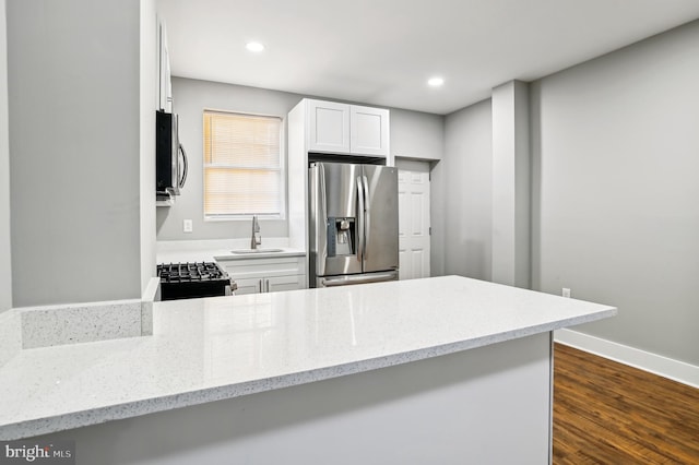 kitchen featuring kitchen peninsula, appliances with stainless steel finishes, dark hardwood / wood-style flooring, light stone counters, and white cabinetry