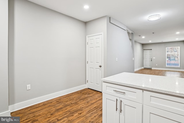 kitchen with light stone countertops, hardwood / wood-style flooring, and white cabinetry