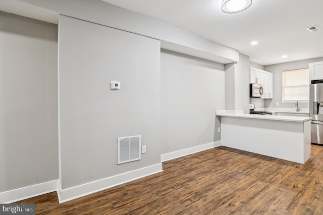 kitchen with kitchen peninsula, stainless steel appliances, sink, hardwood / wood-style flooring, and white cabinetry