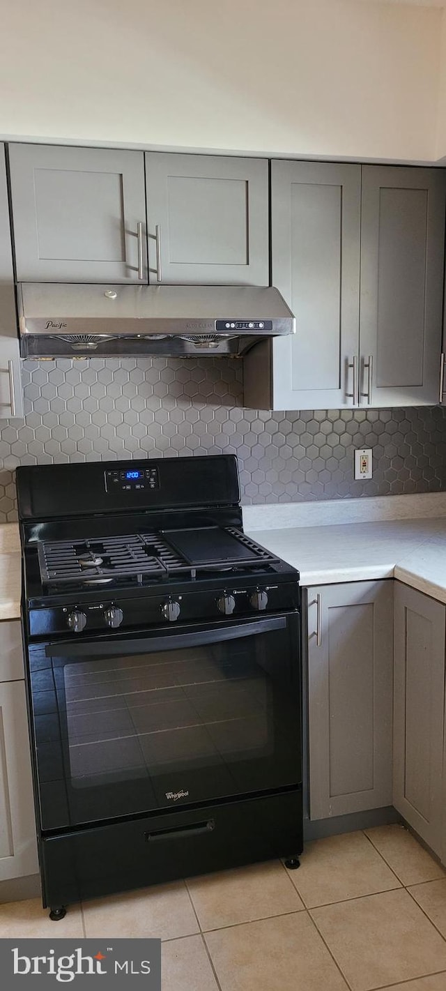 kitchen featuring black gas range, gray cabinetry, and decorative backsplash