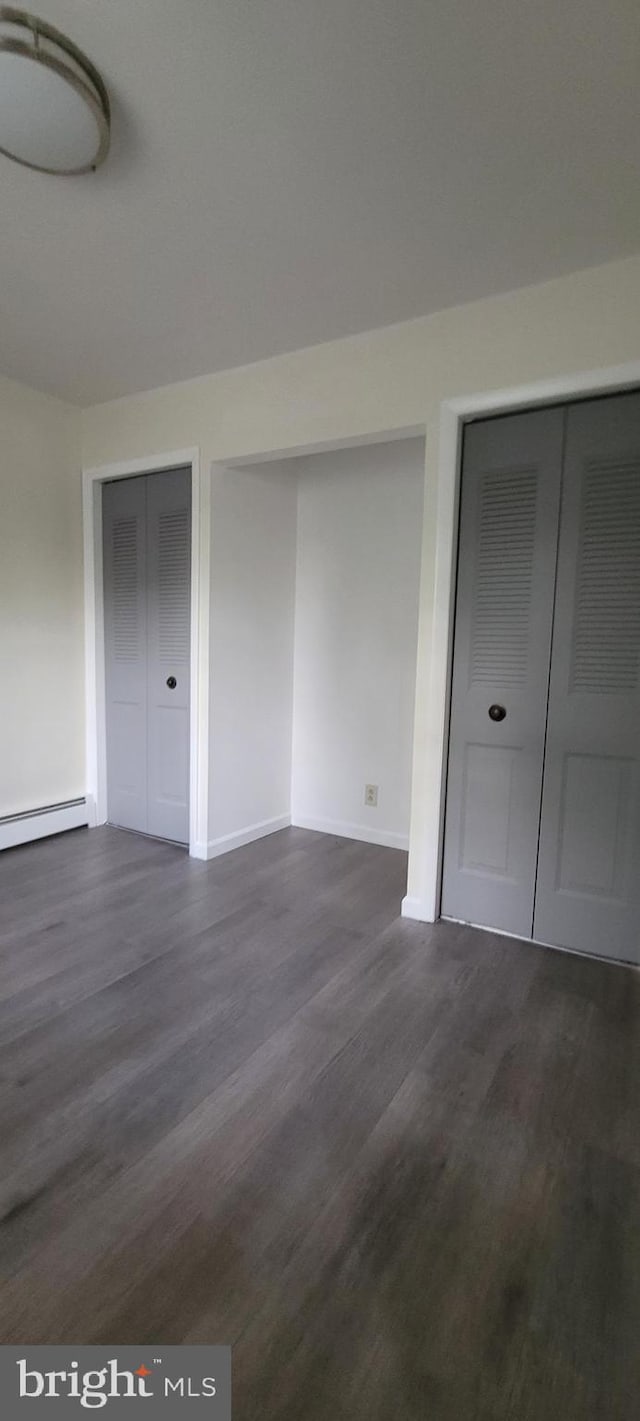 unfurnished bedroom featuring dark hardwood / wood-style flooring, two closets, and a baseboard heating unit