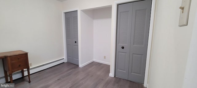 bedroom featuring dark hardwood / wood-style floors, multiple closets, and a baseboard heating unit