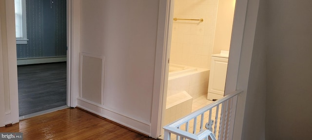 bathroom with hardwood / wood-style flooring, a baseboard radiator, and a bathtub