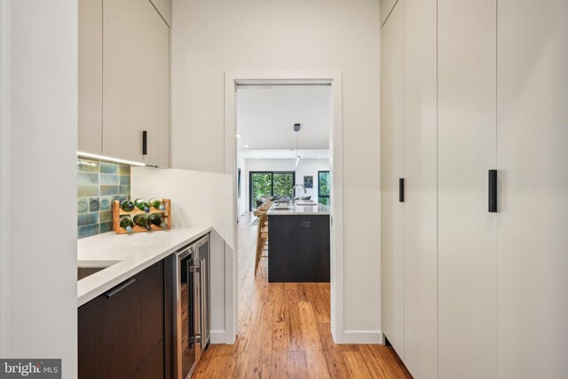 bar area featuring wine cooler, light wood finished floors, and baseboards