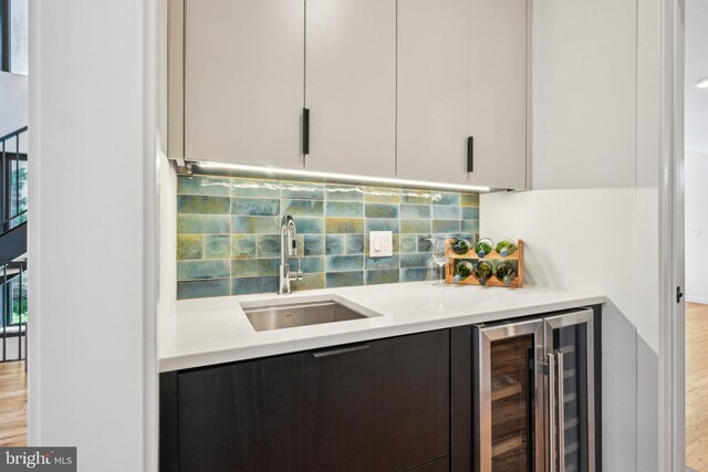 indoor wet bar featuring beverage cooler, tasteful backsplash, and light wood-style flooring