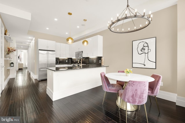 kitchen featuring stainless steel appliances, dark countertops, white cabinetry, and hanging light fixtures