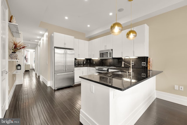 kitchen featuring stainless steel appliances, a peninsula, white cabinetry, dark countertops, and decorative light fixtures