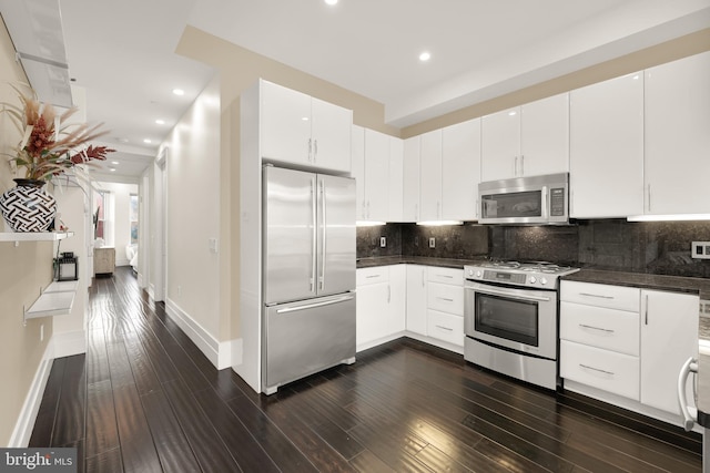 kitchen with appliances with stainless steel finishes, dark wood-style flooring, white cabinets, and backsplash