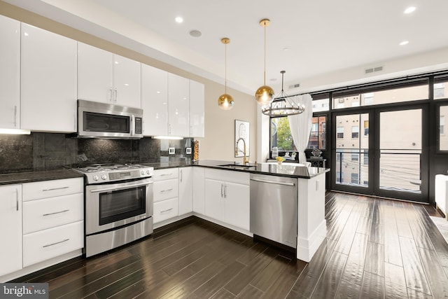 kitchen featuring stainless steel appliances, a peninsula, a sink, white cabinetry, and hanging light fixtures