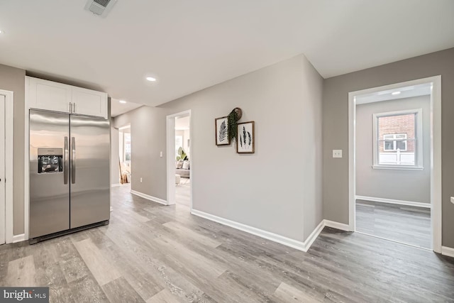 kitchen featuring stainless steel refrigerator with ice dispenser, light wood finished floors, visible vents, white cabinets, and baseboards