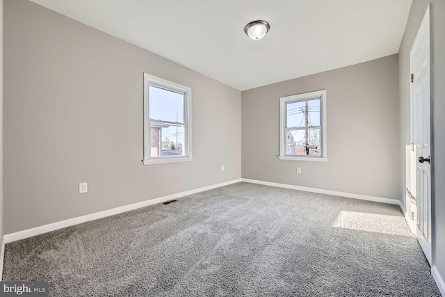 carpeted empty room featuring a healthy amount of sunlight, baseboards, and visible vents