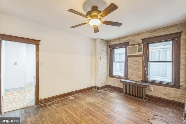 empty room featuring wood-type flooring, an AC wall unit, radiator, and ceiling fan