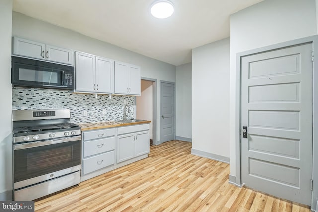 kitchen with stainless steel gas range, sink, light hardwood / wood-style flooring, white cabinets, and butcher block counters