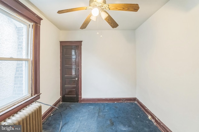 spare room featuring dark colored carpet, radiator heating unit, and ceiling fan