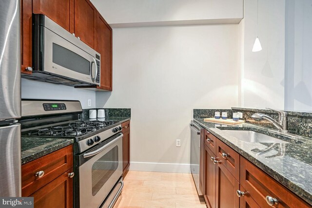 kitchen featuring appliances with stainless steel finishes, light wood-type flooring, dark stone counters, sink, and pendant lighting