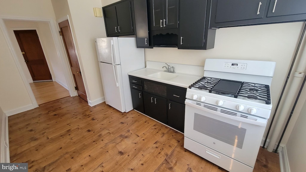 kitchen with a sink, white appliances, light wood-type flooring, and dark cabinets