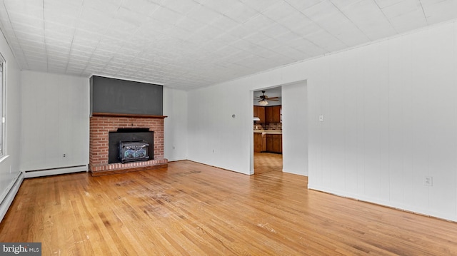 unfurnished living room with a brick fireplace, ceiling fan, and light wood-type flooring