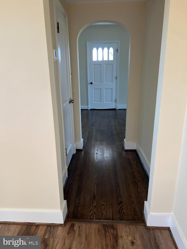 hall featuring arched walkways, baseboards, and wood finished floors