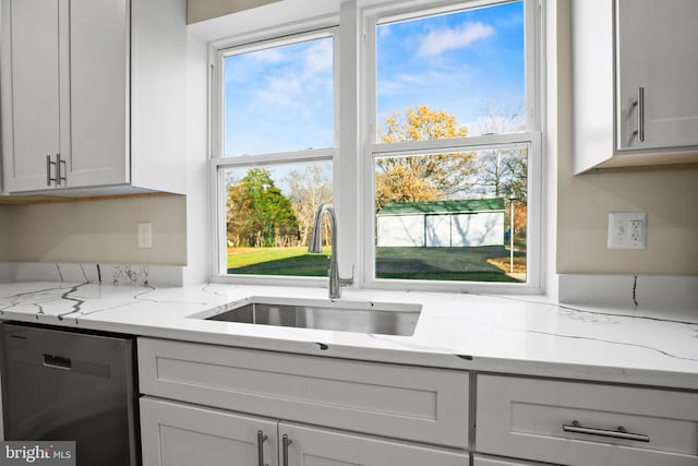 kitchen with light stone counters, dishwasher, and a sink