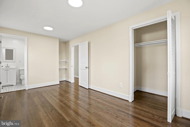 unfurnished bedroom with a closet, a sink, baseboards, and wood finished floors