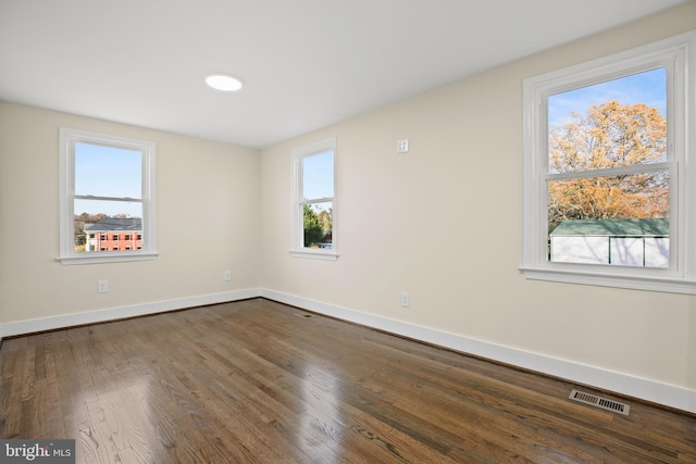 unfurnished room featuring visible vents, baseboards, and dark wood-style floors